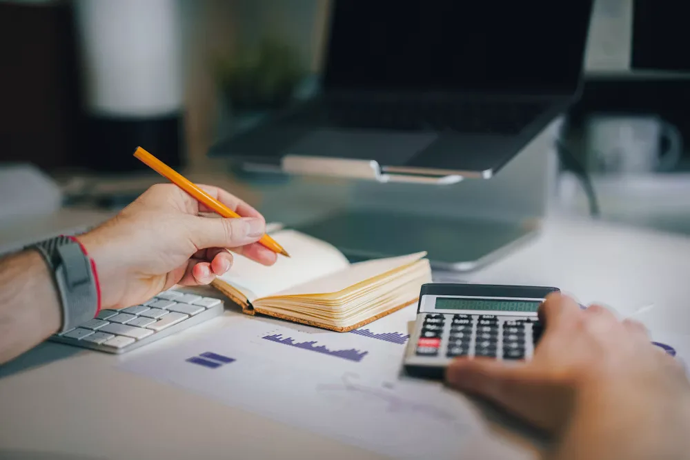 Calculator and notebook used to check savings math on a desk
