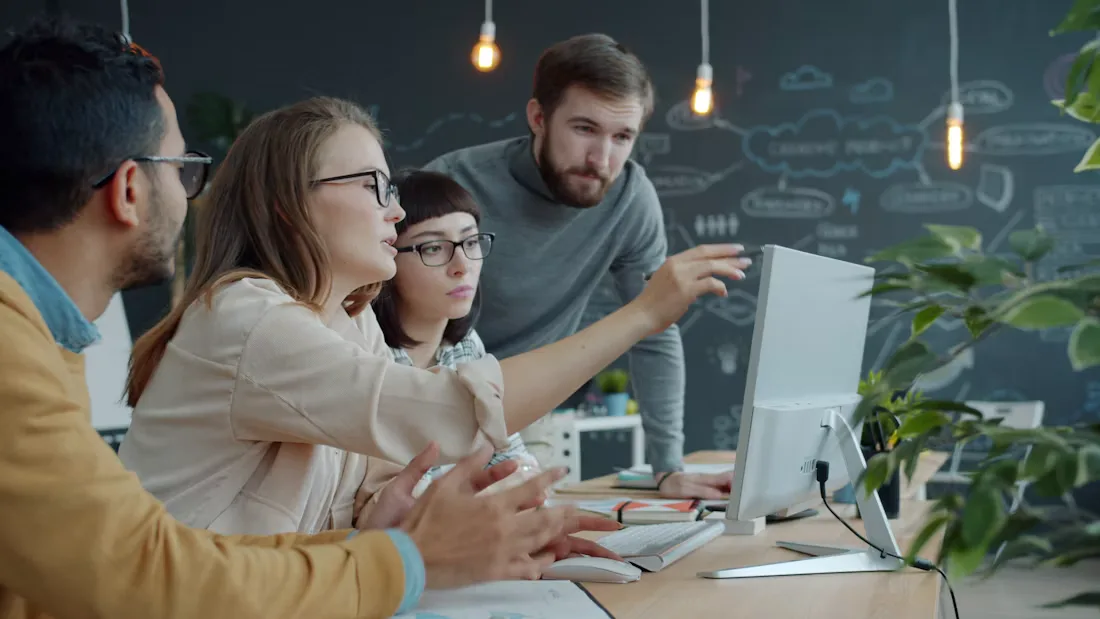 Team collaborating around a computer discussing deal listings in an office